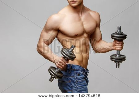 Studio shot of Shirtless bodybuilder holding dumbell and showing his muscular arms.