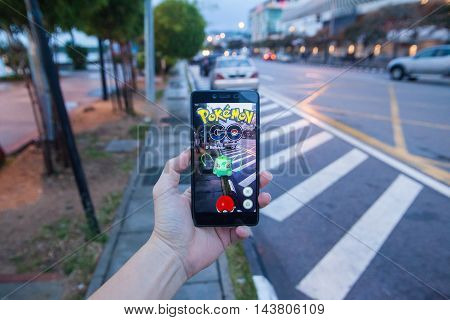 Penang, Malaysia - August 13, 2016 : Man holding a smartphone with his left hand playing Pokemon Go game. Screen on the smartphone is a Pokemon character called 