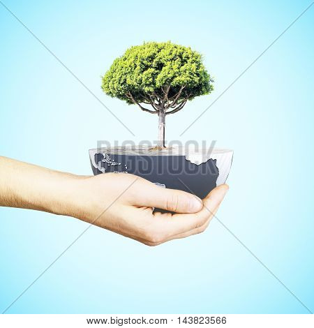 Male hand holding half a globe with large tree on blue background. Green earth concept. 3D Rendering