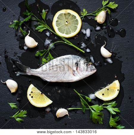Fresh Fish Orata Over a Black stone with vegetables, lemon and pieces of ice. 