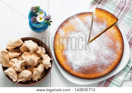 Top view: flowers, brown meringues and manna semolina pie on white wooden table