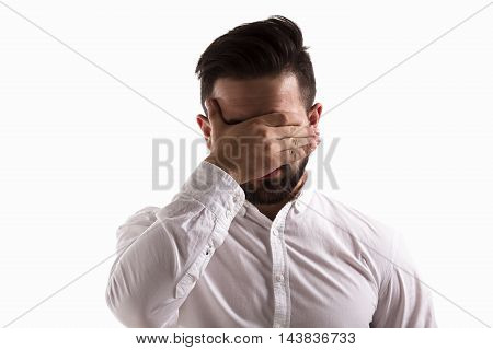 Portrait of embarrassed handsome hispter man closing his eyes isolated on white background. Young man in white shirt in studio.