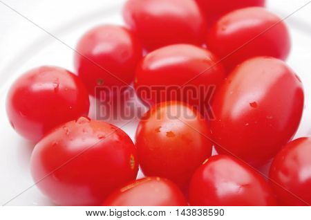 HOMEGROWN PLUM TOMATOES IN VIVID RED. 
Plate of fresh, homegrown and healthy tomatoes on a white background. Delicious, organic, natural food ready to eat.