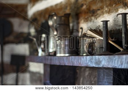 Antique cups sit on shelf in wooden cottage.