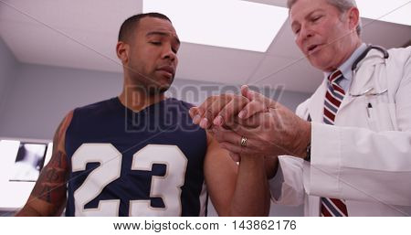 Attractive Male Sports Athlete With Mid Aged Male Doctor Examining Injury