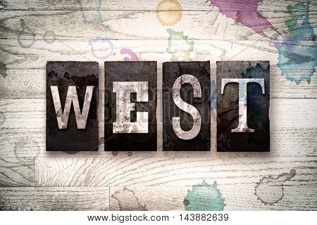 The word "WEST" written in vintage dirty metal letterpress type on a whitewashed wooden background with ink and paint stains.