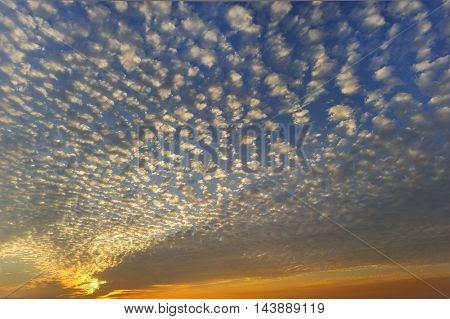 Cloudscape is a bright white pattern of clouds reaching across a beautiful vibrant color filled blue and orange sunset sky.