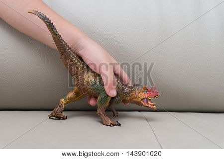 kids hand catching a carnotaurus toy on a sofa at home