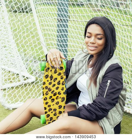 cool pretty smiling afro-american happy young woman with skate board hanging aroung at foothball field smiling