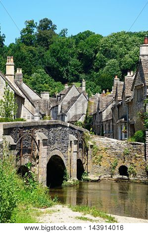 Stone bridge over the river Bybrook with cottages to the rear Castle Combe Wiltshire England UK Western Europe.