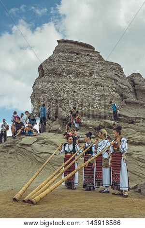 Bucegi Mountains Romania - August 6 2016: Group of young Romanian female artists wearing colorful traditional costumes play the tulnic near the legendary Sphinx megalith in Bucegi mountains.
