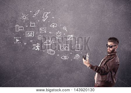 An elegant hipster guy trying to use a vintage camera with camera settings icons drawn on wall, like flash, white balace or ISO value concept