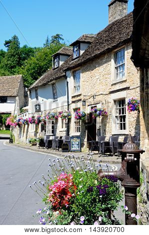 CASTLE COMBE, UNITED KINGDOM - JULY 20, 2016 - Old water pump and flowers wth The Castle Inn to the rear Castle Combe Wiltshire England UK Western Europe, July 20, 2016.