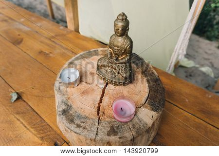 Gold plated Buddha statue standing on a wooden stand and candles in front of him