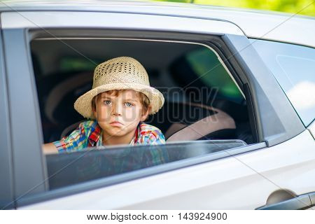Sad little kid boy sitting in car in traffic jam during going for summer vacation with his parents. Tired, exhausted child not happy about journey.
