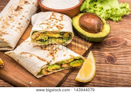 Chicken, avocado and vegetables burrito on the wooden background.