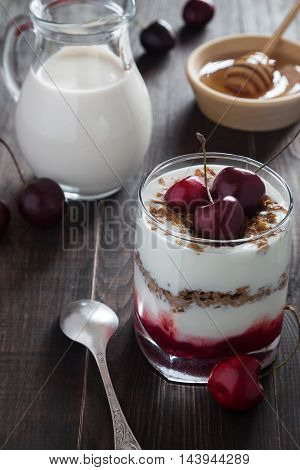 A glass of cherry yoghurt with muesli honey and a jar of milk