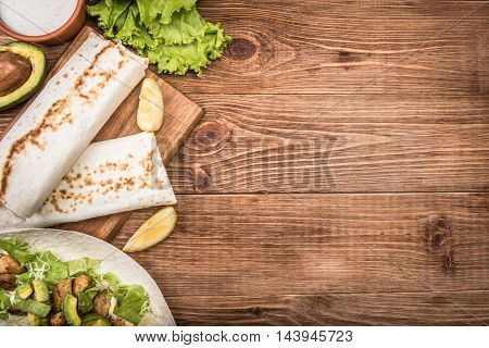 Chicken, avocado and vegetables burrito on the wooden background.