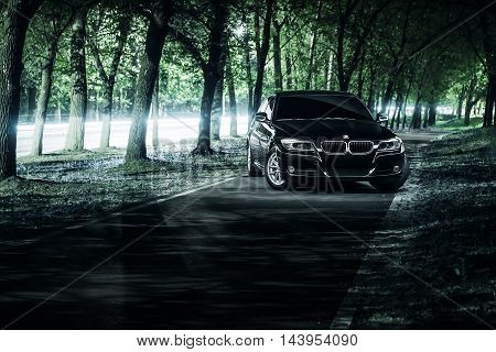 Saratov, Russia - June 12, 2015: Black car BMW E90 stand on road in darkness forest at night