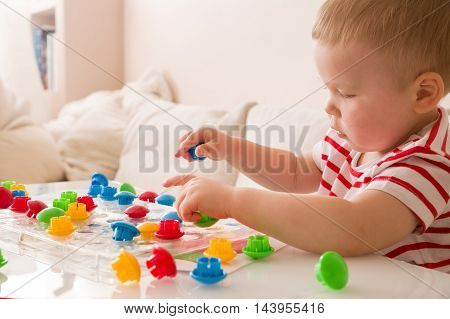 Closeup of child's hand taking bright mosaic parts. Playing and learning colors at home. Toddler boy in a striped shirt playing with colorful constructor details. Activities with children