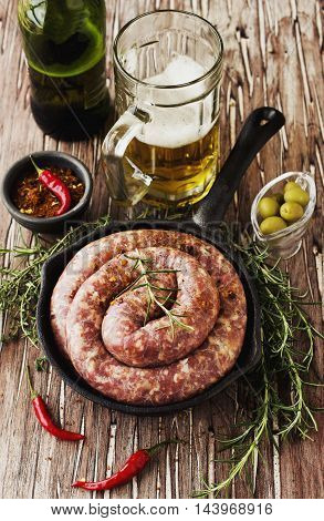 raw beef sausages on a cast-iron pan with rosemary and spices on a wooden table, South African boerewors