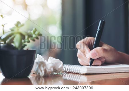 Closeup Image Of A Hand Working And Writing Down On A White Blank Notebook With Screwed Up Papers On