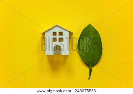 Miniature Toy Model House With Green Leaves On Yellow Colourful Trendy Backgdrop. Eco Village, Abstr
