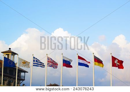 Flags Of Different Countries Flapping In Wind Against Blue Sky