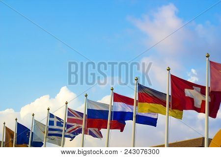 Flags Of Different Countries Flapping In Wind Against Blue Sky