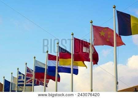 Flags Of Different Countries Flapping In Wind Against Blue Sky