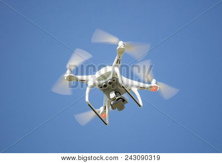 White drone with digital camera, filming from above. Proper for aerial surveillance. Clear blue sky background.