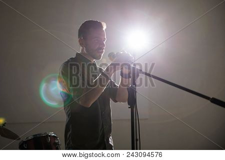 Male Lead Singer Performing Live On Stage With Bright Spotlight In Background