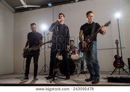 Lead Singer With Guitarist And Drummer Performing On Stage At Music Concert