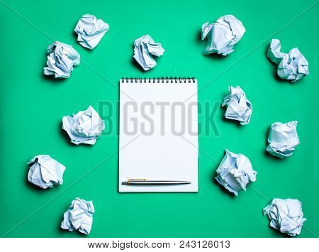 White Notebook With Pen On A Green Background Among Paper Balls. The Concept Of Generating Ideas, In
