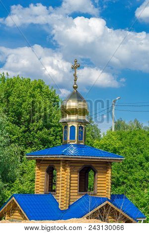 Wooden Orthodox Church With Gilded Domes On A Background Of Green Foliage Of Trees And A Bright Blue