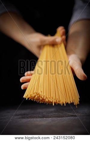 Italian long spaghetti in the hands of the cook on a dark background. The concept of cooking food