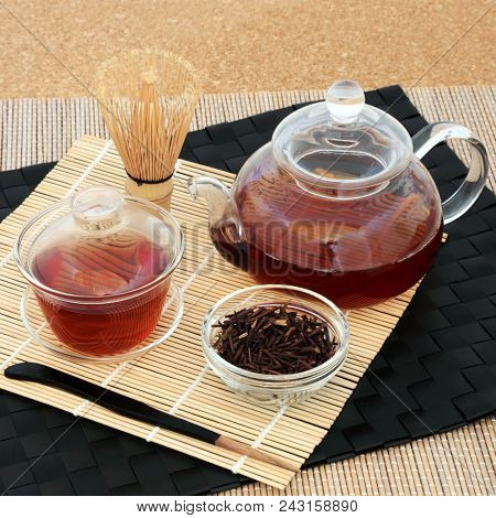 Kuchika Japanese roasted green twig tea for good health with glass teapot and cups, dried twigs, stirrer and whisk on bamboo and cork background. 