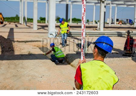 Construction Worker Is Holding Leveling Rod To Help Surveyor, Geodesist To Measure Position, Depth.