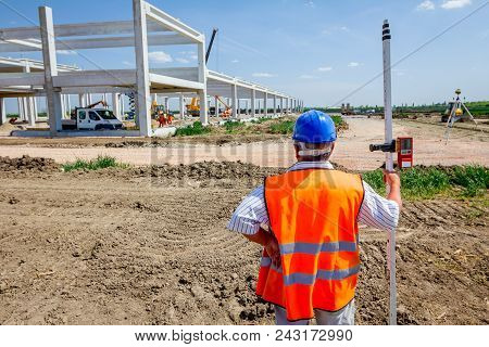 Construction Worker Is Holding Leveling Rod To Help Surveyor, Geodesist To Measure Position, Depth.