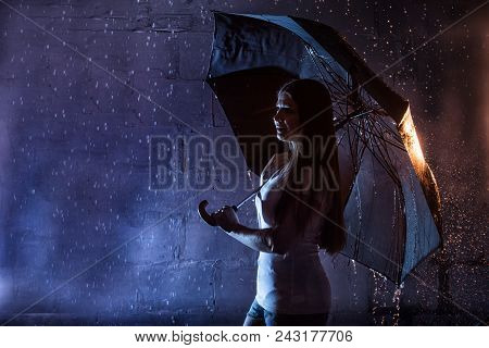 Girl In The White Shirt With Black Umbrella, Water Drops Around And Dark Walls Background Illuminate