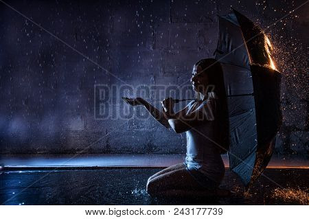 Girl In The White Shirt With Black Umbrella, Water Drops Around And Dark Walls Background Illuminate