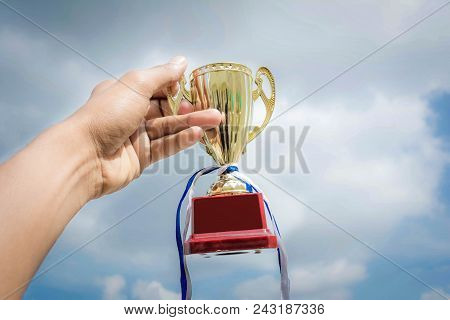 Hand Holding Winner Trophy Cup On Sky Background