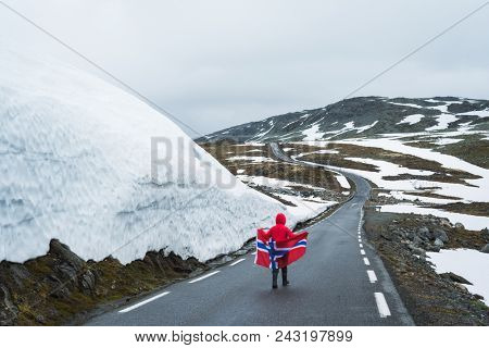 Bjorgavegen - Snowy road in Norway. Girl with the Norwegian flag on a mountain road near a wall of snow. Tourist Route Aurlandsfjellet runs from Aurlandsvangen to Laerdalsoyri