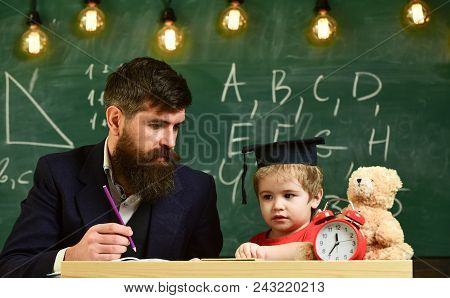 Hometask Concept. Enthusiastic Kid Studying With Teacher. Teacher In Formal Wear And Pupil In Mortar