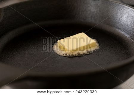 A Butter Pat Melting On A Black Cast Iron Frying Pan.