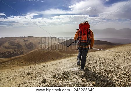 Man With Backpack On Path In Desert Near Neide Volcano On Tenerife Island With Stones And Blue Sky A