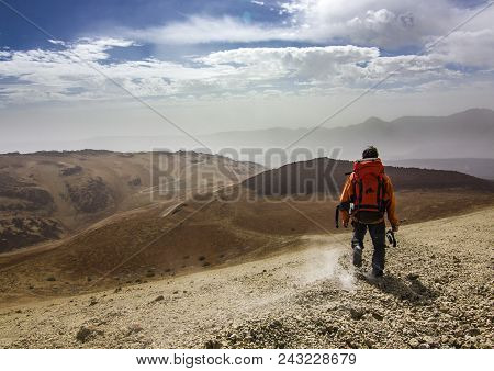 Man With Backpack On Path In Desert Near Neide Volcano On Tenerife Island With Stones And Blue Sky A