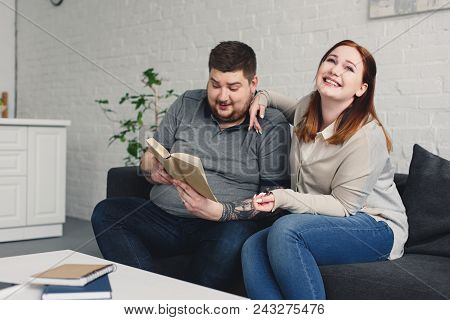 Boyfriend Reading Book To Smiling Girlfriend At Home