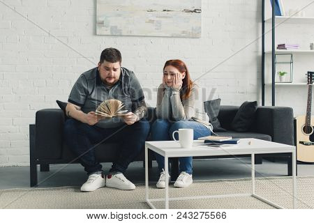 Boyfriend Searching Something In Book, Sad Girlfriend Sitting Near On Sofa