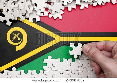 Vanuatu Flag  Is Depicted On A Table On Which The Human Hand Folds A Puzzle Of White Color.